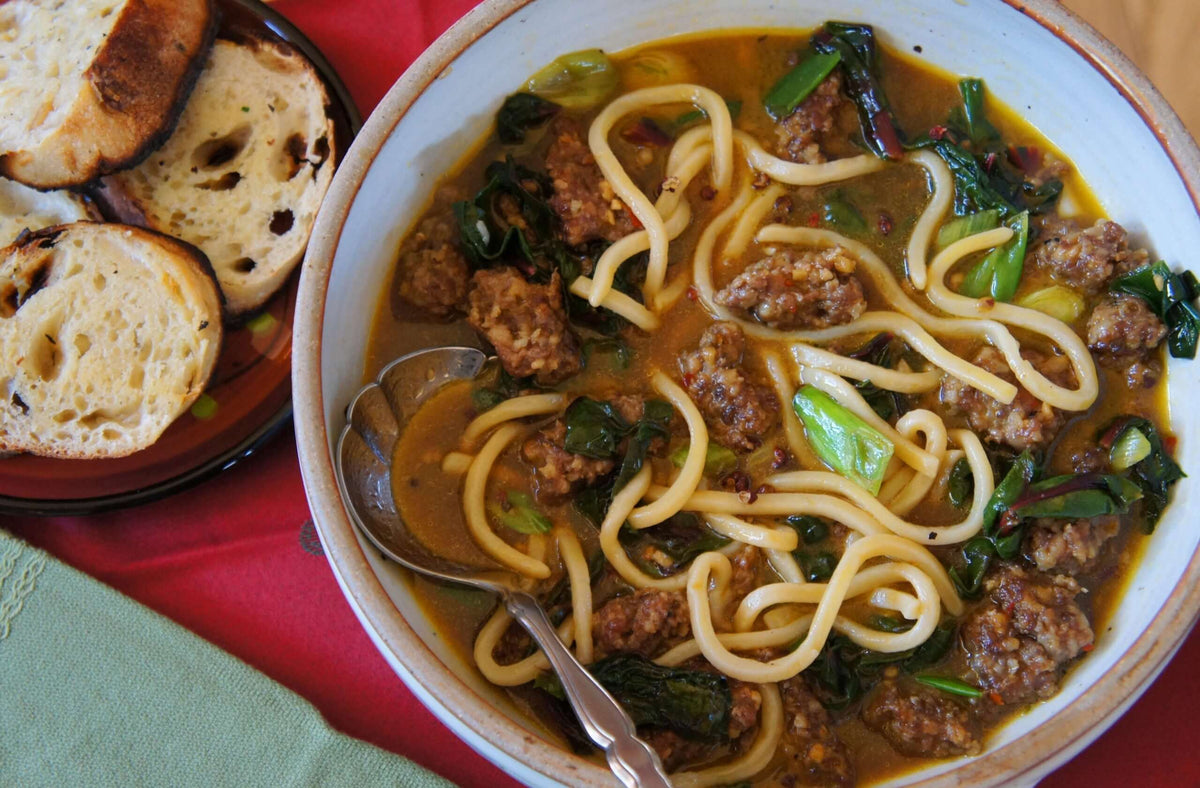 A bowl of spicy pork soup with noodles and grilled bread