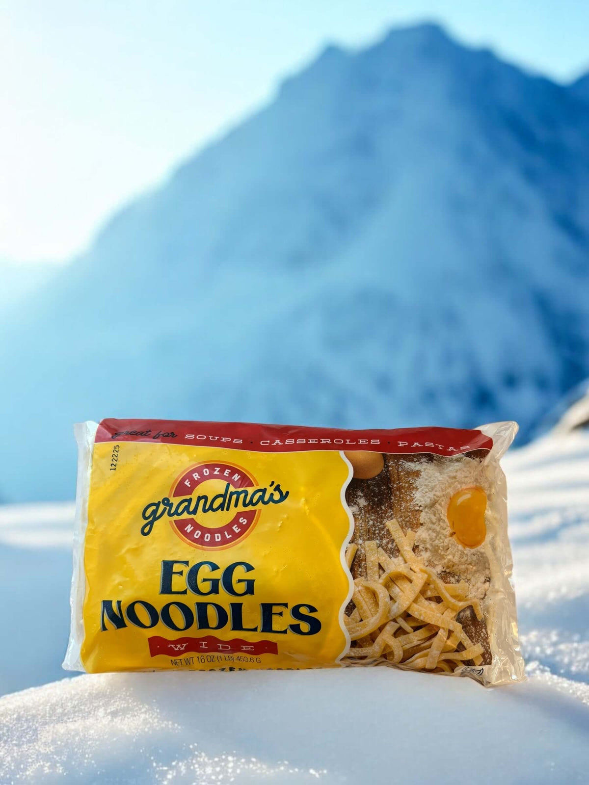 A package of Grandma's Frozen Noodles on snow with a snowy mountain in the background. 