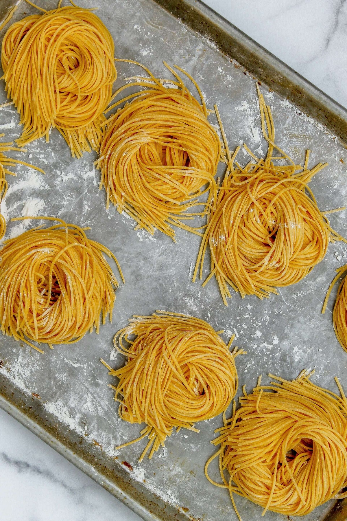 Fresh Spaghetti egg noodles placed on a pan and dusted with flour.