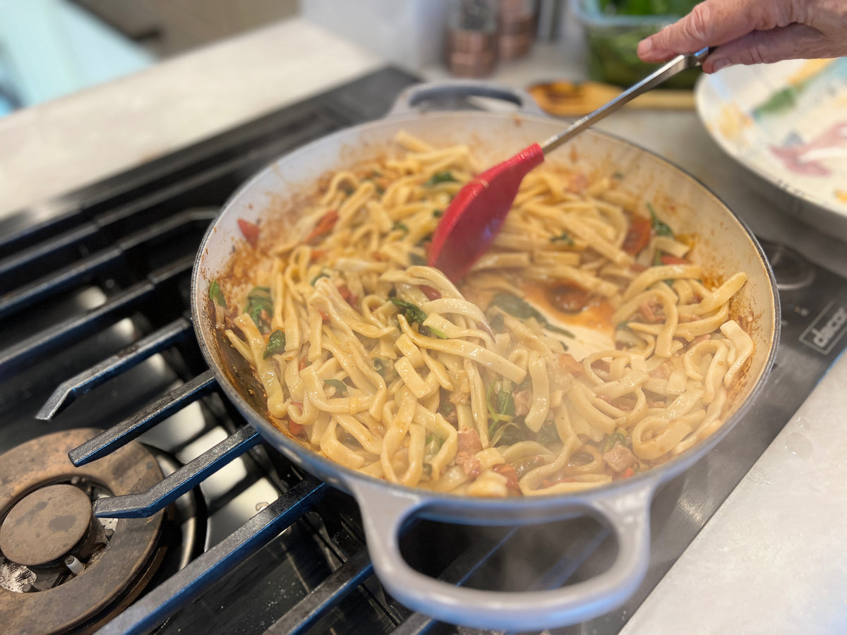 finishing egg noodles in a hot pot with sauce and pasta water.