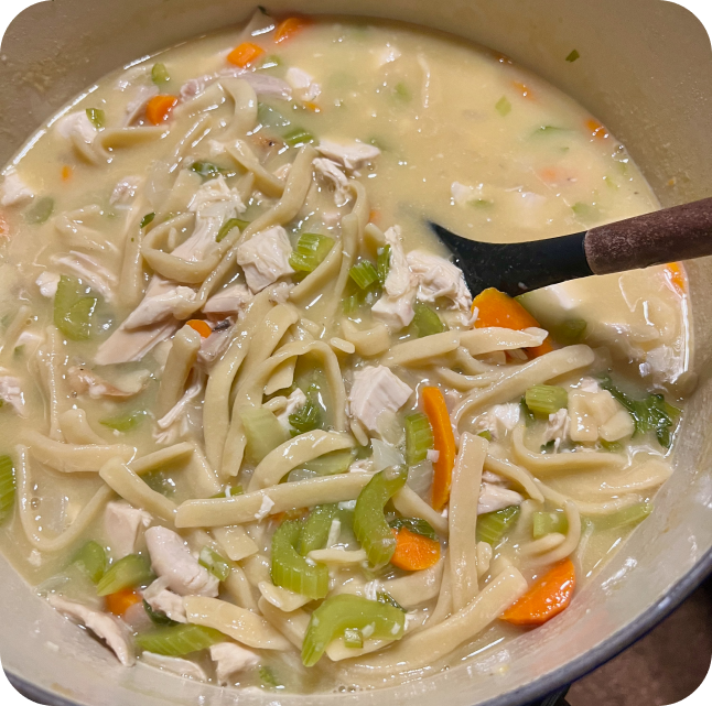 Stirring chicken noodle soup in a dutch oven