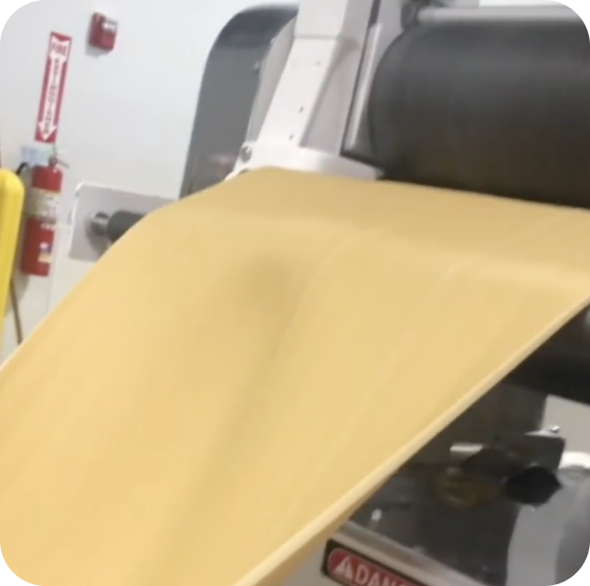 Dough sheet going into rollers, flattening the noodle dough