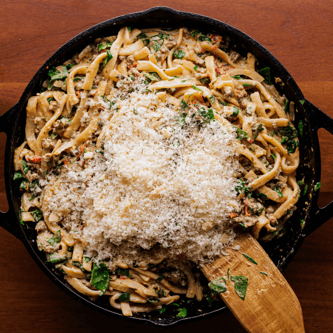 Parmesan grated over the top of fennel sausage egg noodles in cast iron.